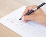 Closeup of hand holding pen and filling out questionary form on table